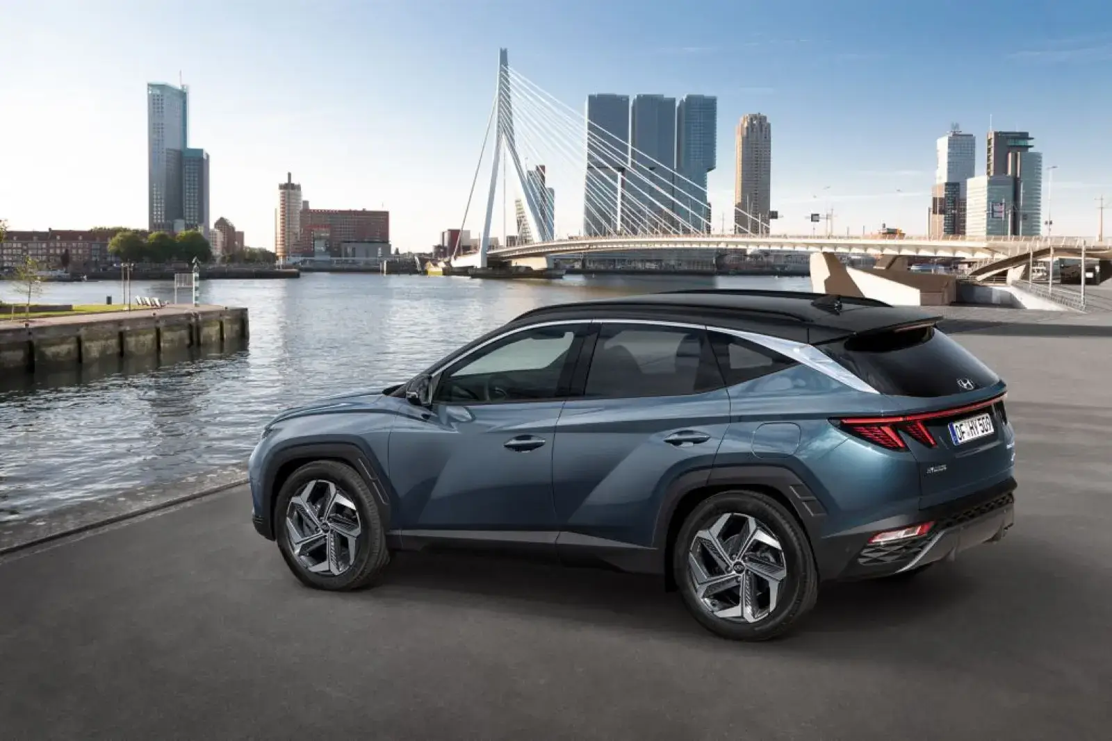 Hyundai Tucson PHEV azul aparcado junto a un río con la ciudad al fondo