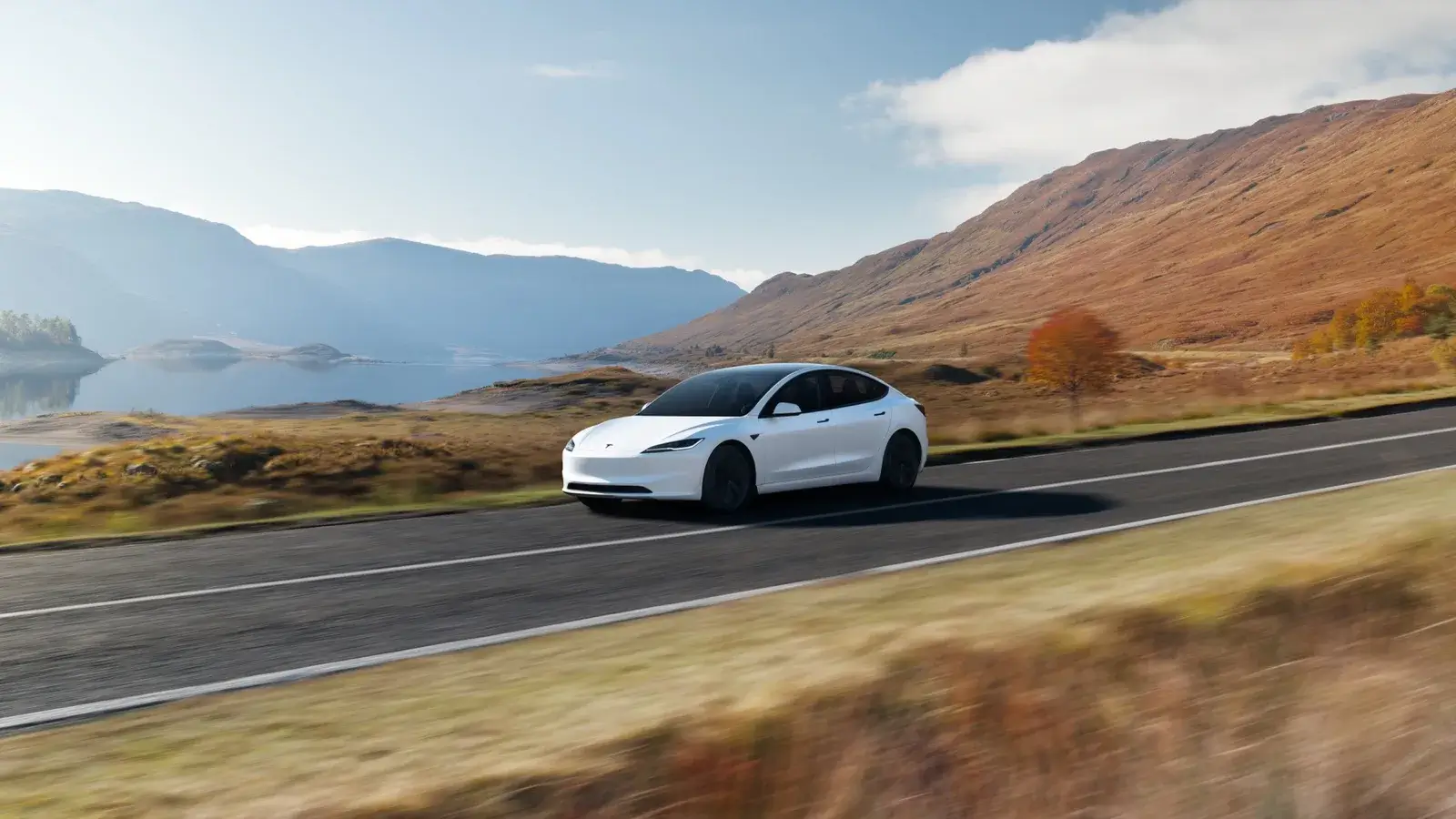 Tesla Model 3 blanco circulando junto a un lago de montaña